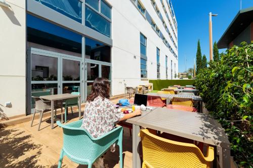 a woman sitting at a table outside a building at ibis budget Huerta De Murcia in Murcia