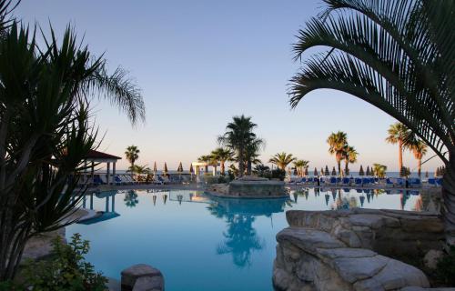 a large swimming pool with palm trees and blue water at Leonardo Cypria Bay in Paphos City