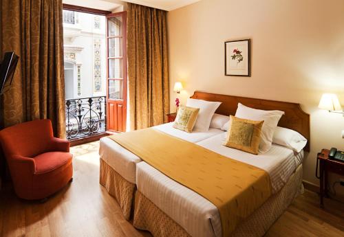 a hotel room with a bed and a chair and a window at Sercotel Las Casas de los Mercaderes in Seville