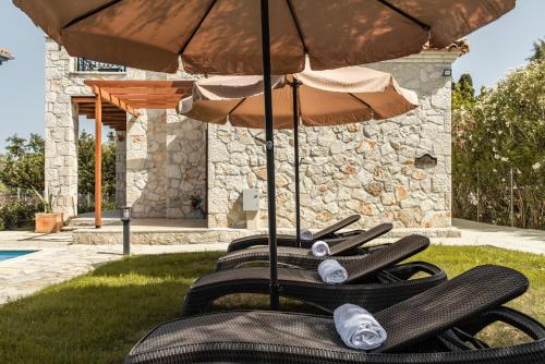 a row of black lounge chairs under an umbrella at Murtini Stone Villa with Private Pool, by ZanteWize in Ayios Kirikos