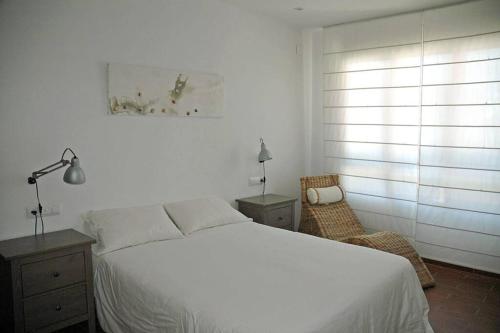 a bedroom with a white bed and a chair at Villa with pool, 200m from beach in Cala Blanca