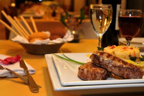 a plate of food with meat and a glass of wine at Orquideas Hotel & Cabañas in Puerto Iguazú