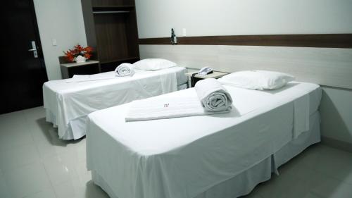 two beds in a room with white sheets and towels at Tezla Hotel in Primavera do Leste