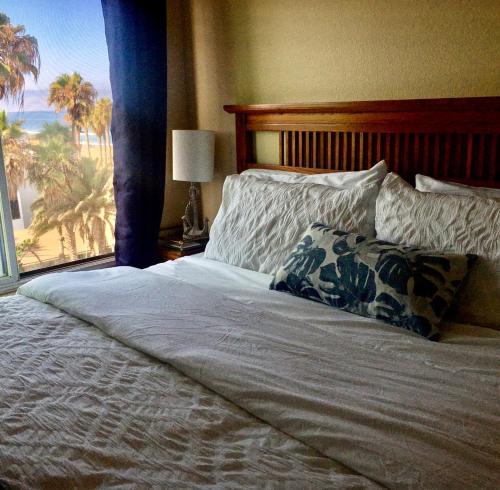 a bed with a pillow and a window with palm trees at See By The Sea in San Diego