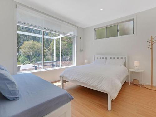 a white bedroom with two beds and a window at Banksia on Blenheim by Experience Jervis Bay in Vincentia