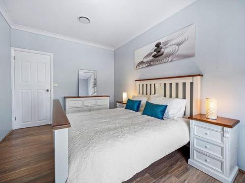 una camera da letto con un grande letto bianco con cuscini blu di Vincentia Breeze by Experience Jervis Bay a Vincentia