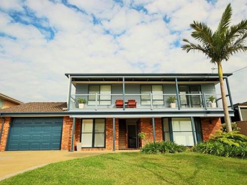 a house with a palm tree in front of it at Benjos by Experience Jervis Bay in Vincentia