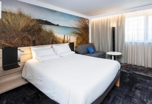 a bedroom with a large white bed and a couch at Novotel Rennes Alma in Rennes