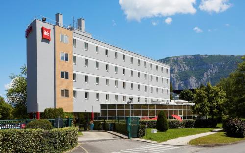 un grand bâtiment blanc avec une montagne en arrière-plan dans l'établissement ibis Archamps Porte de Genève, à Archamps