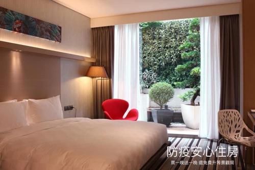 a bedroom with a bed and a red chair in front of a window at Taipei 101 SPARKLE Hotel in Taipei