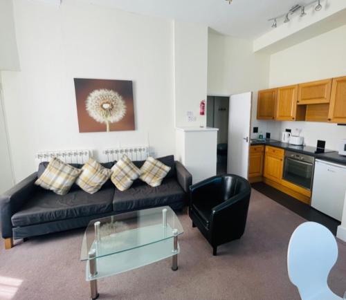 a living room with a black couch and a kitchen at Devonshire House Holiday Flats in Eastbourne