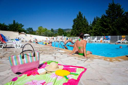 a woman in a bikini sitting next to a swimming pool at Ludocamping in Lussas