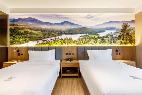 twee bedden in een hotelkamer met een schilderij aan de muur bij TRUE Go hotel in Chengdu