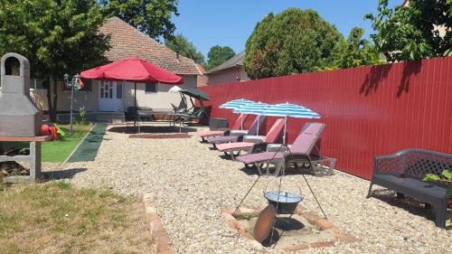 a row of patio chairs with umbrellas and a red fence at Casa Lyna in Gyomaendrőd