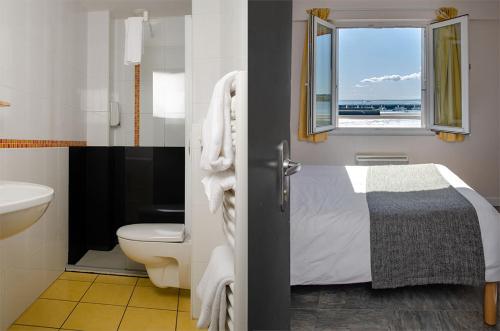 a bathroom with a bed and a toilet and a window at Hôtel & Restaurant de la Plage in Crozon