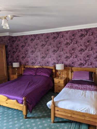 two beds in a bedroom with purple wallpaper at The Londesborough Arms bar with en-suite rooms in Market Weighton