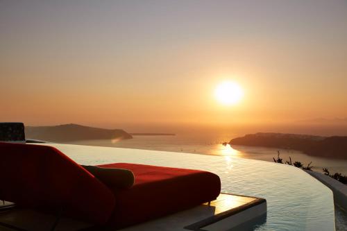 a sunset on a pool with a couch on the edge at White Pearl Cavalieri in Imerovigli