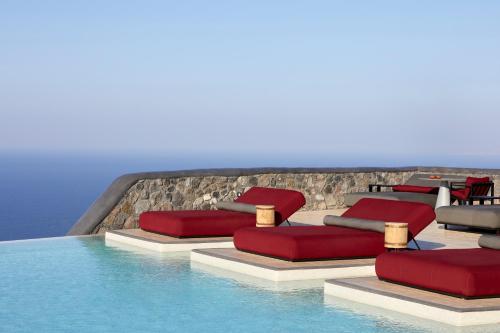 einen Pool mit roten Kissen und Stühlen neben dem Wasser in der Unterkunft White Pearl Cavalieri in Imerovigli