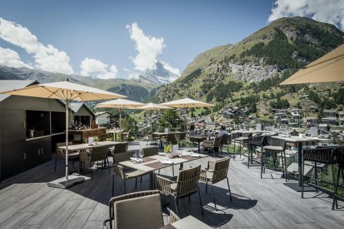 采爾馬特的住宿－Petit Chalet by Schönegg，餐厅配有桌椅,位于山脉的背景中