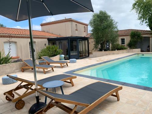une piscine avec des chaises longues et un parasol dans l'établissement Le Chant des Pierres - Entre Terre et Mer, à Pornic