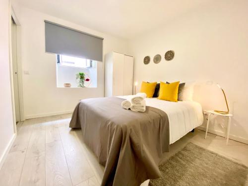 a white bedroom with a large bed with yellow pillows at BrightHouse - Modern Apartments in Sítio Nazaré in Nazaré