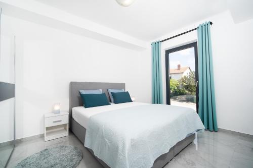 a white bedroom with a large bed with blue pillows at Villa Apartments Lela in Rabac