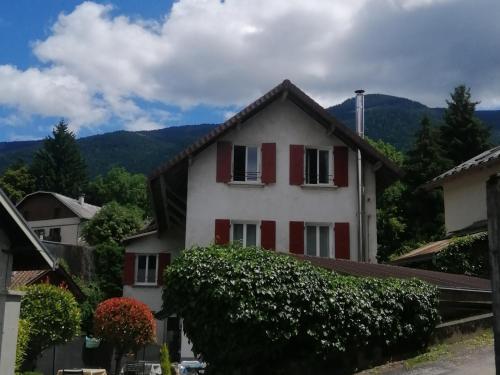 a white house with red shutters and mountains in the background at GÎTE REDROOSTER HOME - 160m2, 4 ch, 2 sdb, fibre, parking, sauna, bain à remous in Theys