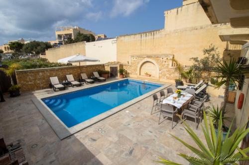 einen Pool mit einem Tisch und Stühlen neben einem Gebäude in der Unterkunft Villa Mandolina in Għarb