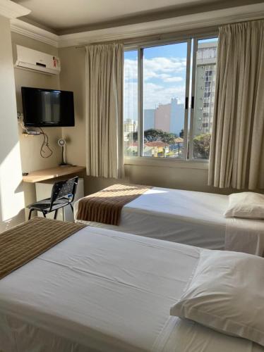a hotel room with two beds and a window at Hotel Desbravador in Chapecó