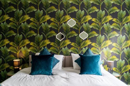 a bed with blue pillows in a bedroom with a tropical wallpaper at BEAUTIFUL Contractor and Family House - M18 & A1 - Private Parking & Big Garden in Doncaster