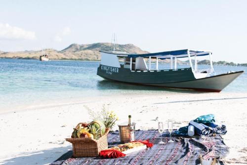 a picnic on a beach with a boat in the water at The Seraya Resort Komodo in Labuan Bajo