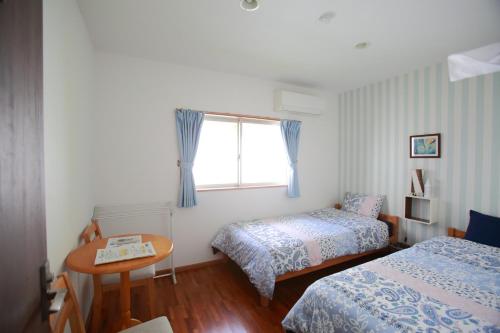 a bedroom with two beds and a table and a window at Tanegashima Minshuku Hapisuma in Minamitane