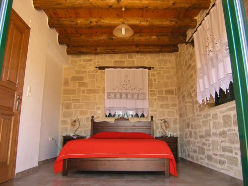 1 dormitorio con cama roja y pared de piedra en Stratos Villas, en Kaloniktis