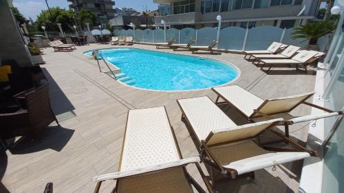 una piscina con sedie a sdraio e un mucchio di accessori di Hotel Caesar Paladium a Rimini