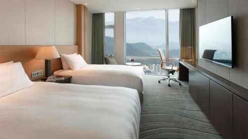 a hotel room with a bed, chair, desk and a television at LOTTE City Hotel Jeju in Jeju
