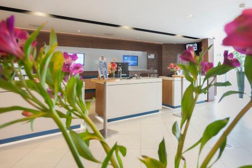 a lobby with a counter with pink flowers in the foreground at Novotel Rotterdam - Schiedam in Schiedam