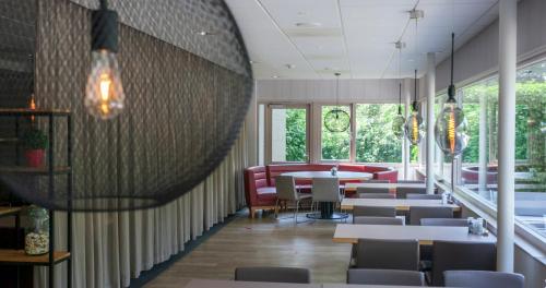 a dining room with tables and chairs and windows at Novotel Rotterdam - Schiedam in Schiedam