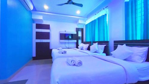 two white beds in a room with blue lighting at Railview Residency in Alleppey