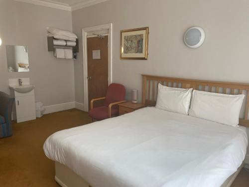 a bedroom with a white bed and a red chair at Brookside Lodge in Baldock