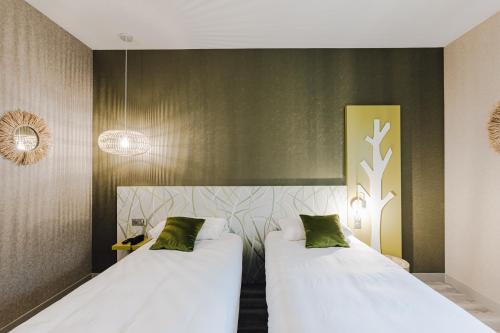 two beds in a hotel room with white sheets and green pillows at ibis Styles Contres-Cheverny in Le Controis En Sologne