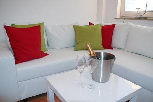 Un sofá blanco con almohadas rojas y verdes y una botella de champán. en Premium Ferienwohnung Sonnenaufgang en Witzenhausen