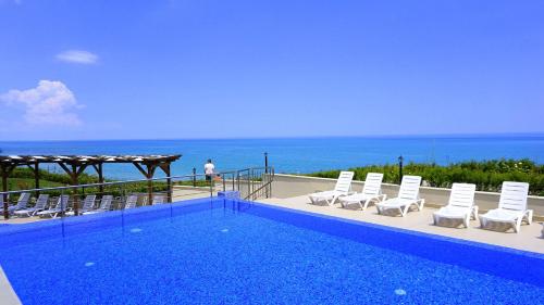 a swimming pool with chairs and the ocean in the background at Бяла Клиф Форест - Byala Cliff Forest in Byala