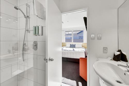a bathroom with a shower and a sink and a bed at The Hotel Nelson in Nelson