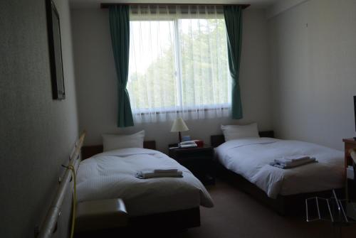 two beds in a hotel room with a window at Highland Furano in Furano