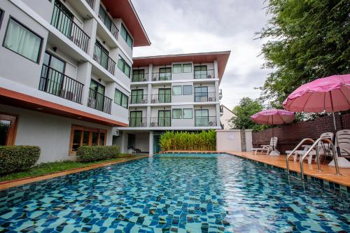 a swimming pool in front of a building with an umbrella at Huen Jao Ban Hotel in Chiang Mai