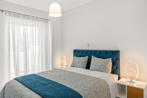 a white bedroom with a blue bed and a window at BillyMare central Glyfada apartment in Athens
