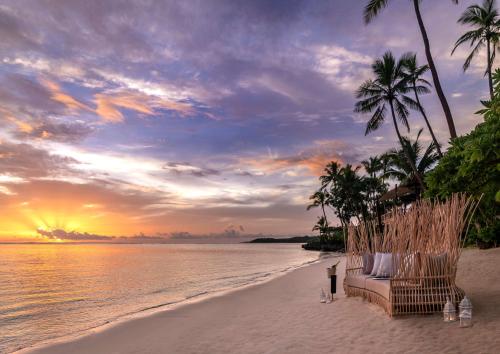 einen Strand mit Couch und Palmen und Sonnenuntergang in der Unterkunft Shangri-La Yanuca Island, Fiji in Voua