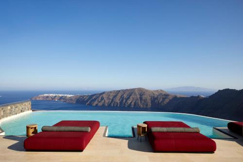 a swimming pool with two red chairs and a view at White Pearl Cavalieri in Imerovigli