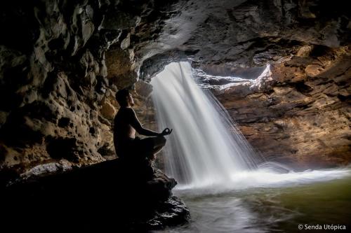 a man sitting on a rock in front of a waterfall at Wisdom Forest Lodge in Tena