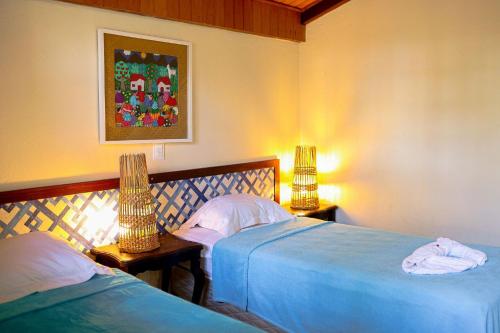 two beds in a bedroom with two lamps on tables at Pousada Villa di Milos - By Quarto à Vista in Pipa